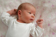 © sementsova321 - A newborn baby rests on a soft blanket while observing the surroundings. The baby is dressed in a simple white outfit and shows curiosity with bright eyes