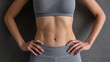 © pecherskiydotkz - Close-up of a toned midsection in gray athletic wear against a textured background, highlighting strength, fitness, and dedication to health.