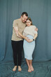 © DSMT - Couple stands close together, sharing joy during maternity shoot in a studio with a blue backdrop, highlighting their excitement for their upcoming baby