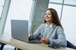 © DSMT - Woman at desk works on laptop and smiles while holding glasses in a modern office setting during daytime