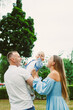 © DSMT - Parents lift their baby in a park while smiling during an outdoor family gathering on a sunny day in spring