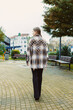 © DSMT - Woman walks in park wearing a patterned outer garment with fringe near benches and buildings during cloudy day