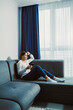 © DSMT - Woman sits on couch in living room looking at smartphone during afternoon