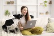 © New Africa - Smiling woman with laptop and her adorable dog on sofa at home