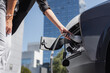 © 24K-Production - Woman connects a charging cable to an electric vehicle in an urban area during daylight.