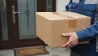 © Moopingz - A close-up shot of a courier in a blue uniform holding a large, taped cardboard delivery box near a residential entrance door.