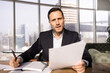 © fizkes - Serious young Latin executive man talking on online video conference call, speaking at camera, holding paper documents, writing notes in notebook, holding corporate meeting. Head shot portrait