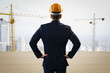 © Who is Danny - Rear view of businessman in suit and helmet looking at construction site with cranes on cityscape background, symbolizing building development vision.