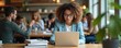 © Viktor - Woman with curly hair wears glasses using laptop at table in cafe. People work and study in coffee shop background. Students collaborate indoors with books and devices.