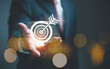 © Chaiwat - Businessman holding a glowing digital target icon with an arrow, symbolizing goal achievement, marketing strategy, and precision business planning in the digital age.