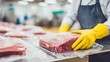 © AGI Studio - A person in yellow gloves handles vacuum-sealed meat packages in a professional kitchen or food processing environment.