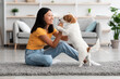 © Prostock-studio - Cheerful young asian woman training her fluffy dog jack russel terrier at home, giving treats for success and smiling, side view, copy space. Obedience training for dogs concept