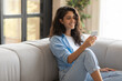 © Prostock-studio - Positive millennial Caucasian woman sitting on couch, using smartphone, surfing web, chatting online, watching video, having remote meeting, messaging with friend at home, free space