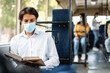 © Prostock-studio - Portrait of focused handsome guy in white shirt and surgical mask sitting near window in public transportat, reading paper book, enjoying fiction story or educational literature, selective focus