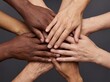© Meow Creations - Top view of diverse hands stacked together in a circle symbolizing unity and teamwork on dark grey