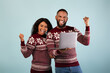 © Prostock-studio - Wow x-mas offer. Overjoyed african american couple celebrating success with laptop, wearing Christmas sweaters and raising fists with joy over blue studio background