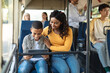 © Prostock-studio - Travel, Tourism, Family And Transportation Concept. Portrait of smiling young black woman and boy sitting and going on a bus, lady hugging son using tablet playing video game or watching video movie