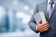 © grey - Professional businessman holding a book or document in a modern office environment, representing knowledge, learning, and corporate responsibility.