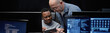 © Seventyfour - Header of young Black man and middle aged Caucasian man collaborating while using digital tablet in modern control room, multiple computer monitors displaying data and security feeds