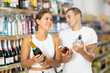 © JackF - Couple of young man and young woman shoppers choosing champagne whiskey and vodka in grocery store