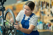 © JackF - Young woman bicycle repair service worker in uniform oiling bicycle wheel
