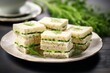 © nsit0108 - Cucumber sandwiches with cream cheese and fresh dill resting on a white plate