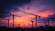 © Suparat - Silhouette of construction tower cranes against a dramatic purple and orange sunset sky. Urban development background.