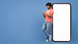 © Prostock-studio - A man stands next to a large blank screen while holding a mobile device. He appears to be engaged and smiles as he looks down at the phone. The background is bright blue.