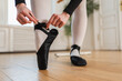 © Юлия Завалишина - Ballerina puts on pointe shoes on leg in dance class. Classical ballet dancer woman in dance studio. Ballerina putting on tying classical pointe shoes for dance training. Ballet school concept