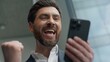 © Yuliia - Close up happy smiling Caucasian middle-aged business man winning with mobile phone online bet casino success victory in office excited businessman male manager employer satisfied with smartphone win