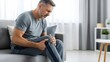© Artfinity - Knee injury and chronic joint pain symptoms. Healthcare and physical therapy needs. Mature man sitting on a sofa holding his painful knee with an expression of discomfort