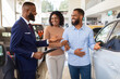 © Prostock-studio - Happy Black Couple Talking To Salesman While Choosing New Car In Dealership Center, Smiling African American Spouses Purchasing Family Vehicle In Modern Automobile Showroom, Closeup Shot