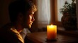 © Bussakon - A man gazes thoughtfully at a lit candle in a dimly lit room bathed in warm golden light