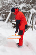 © Chebotaeva Ekaterina - A man in an orange tracksuit clears snow from the paths near the house. An orange snow shovel.
