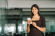 © Stock 4 You - Smiling Latin Hispanic mature female businesswoman holding smartphone in office trading app, working online. Young Indian business woman manager ceo using cell phone mobile application. Copy space
