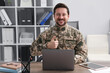 © New Africa - Military education. Student in soldier uniform showing thumbs up at wooden desk in office