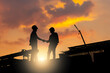 © iPoguz - Silhouette of construction workers shaking hands at industrial site during sunset, Business partnership agreement between engineers at infrastructure construction site, Teamwork and success concepts