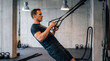 © Николай Срибяник - Fit male athlete performing suspension row exercise using black straps in modern gym with concrete walls and industrial lights for strength training