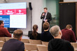 © Anton Gvozdikov - Audience sits in rows while speaker presents at conference. Large screen displays data and charts. Attentive participants in business attire engage with talk in corporate setting.