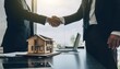 © luzaein - Business partners shaking hands over a model house, symbolizing real estate deal success