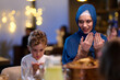 © .shock - Muslim Mother and Son Praying Before Iftar Meal at Home or Restaurant - Religious Traditions, Ramadan Kareem, and Family Bonding Concept.