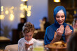 © .shock - Muslim Mother and Son Praying Before Iftar Meal at Home or Restaurant - Religious Traditions, Ramadan Kareem, and Family Bonding Concept.