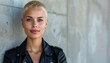 © Roberto - a blonde woman model with shaved hair wearing a black leather jacket standing with a white wall on background, fashion photography, spring summer collection