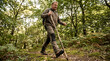 © OlgaNeuroArt - Middle-aged man hiking on a forest trail with a wooden walking stick. Active person trekking in the woods for outdoor adventure and exercise