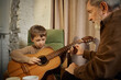 © master1305 - Senior mentor showing guitar chords to young boy at home. Concept of step by step learning, music instruction, family mentoring, creative education, skill transfer.