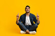 © Prostock-studio - Stylish millennial arab guy in denim sitting on floor, pointing up with both hands at copy space for advertisement or text and smiling, young middle eastern man posing on yellow studio background
