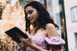 © BullRun - Profile of Hispanic woman with curly hair using digital tablet outdoors, floral dress, symbolizing concentration, freelance career, and empowerment in modern connected lifestyle.