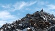 © Bussakon - A lone worker in a hard hat sits atop a vast chaotic mountain of scrap metal under a bright blue sky with clouds