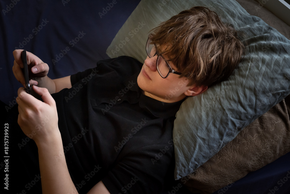 Unhappy stressed teenager boy lyuing down with smartphone