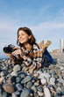 © SHOTPRIME STUDIO - Woman photographer lying among smooth pebbles on a sunny beach with a camera, capturing a candid moment in outdoor lifestyle photography near the coast and sea horizon